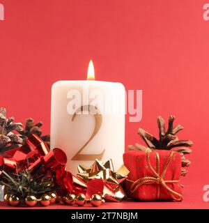 Candela secondo Avvento brucia, candela bianca con il numero due su uno sfondo rosso, decorazione di Natale, spazio per il testo Foto Stock