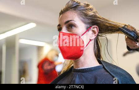 Donna che indossa la maschera viso rossa ottenere fresco taglio di capelli a un parrucchiere durante la pandemia di covid-19 Foto Stock