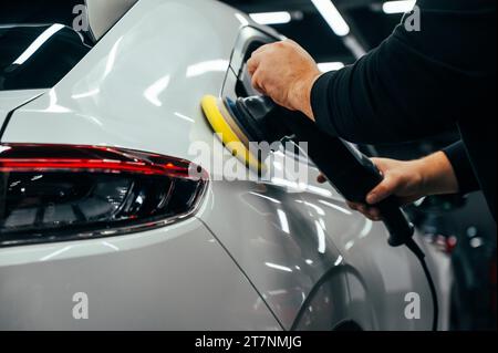 Processo di lucidatura della superficie bianca della carrozzeria della vettura con una lucidatrice orbitale. Foto Stock