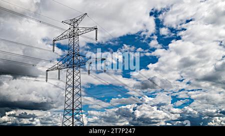 Profilo della parte superiore della torre di trasmissione su sfondo cielo blu e nuvole bianche. Primo piano della struttura a traliccio di piloni elettrici e dei cavi ad alta tensione. Foto Stock