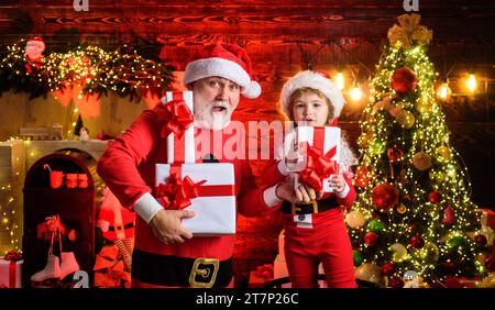 Vigilia di Natale. Sorpresi Babbo Natale e bambino con un regalo di Natale. Vacanze in famiglia e infanzia. Ragazzino e uomo barbuto in costume di Babbo Natale Foto Stock