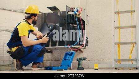 Un tecnico qualificato incaricato della manutenzione ordinaria del sistema hvac esterno, alla ricerca di problemi relativi al refrigerante. Tecnico qualificato che esegue l'ispezione del condizionatore d'aria, scrivendo i dati sul tablet Foto Stock