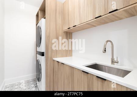 Una lavanderia con armadi di legno, un ripiano in marmo bianco, pavimento in piastrelle a motivi geometrici e lavatrice e asciugatrice bianche Foto Stock