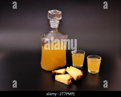 Liquore all'ananas in due bicchieri e una bottiglia su fondo nero, accanto a pezzi di frutta matura. Primo piano. Foto Stock
