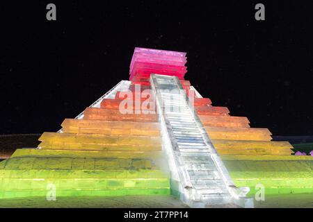 HARBIN, CINA - 1° gennaio 2022: Costruzione di ghiaccio a forma di piramide messicana. Harbin International Ice and Snow Festival. I turisti sono in visita. Loca Foto Stock