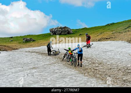 Gli appassionati di mountain bike spingono la loro mountain bike su un campo di neve, Montriond, Chablais, Francia Foto Stock