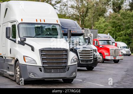 Trasportatori lunghi industriali diversi trattori per semirimorchi grandi con semirimorchi carichi in fila nel parcheggio dell'area di sosta stradale Foto Stock