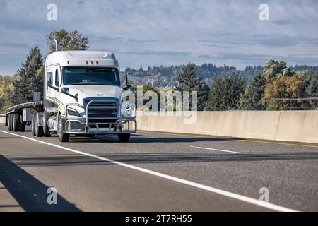 Carro di perforazione grande con supporto a basso profilo bianco per il trasporto di semirimorchi a pianale piatto su strada autostradale con cavalcavia a senso unico con tr autunnale giallo Foto Stock