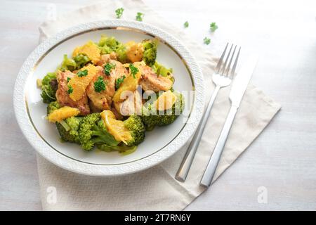 Filetto di pollo all'arancia su verdure di broccoli con contorno di prezzemolo, servito su un piatto bianco, pasto proteico sano per una dieta a basso contenuto di carboidrati, spazio copia, selezionare Foto Stock