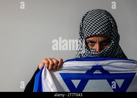 Donna dagli occhi verdi con un velo palestinese che porta una bandiera israeliana. Concetto di conflitto Foto Stock