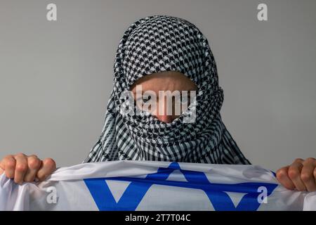 Donna dagli occhi verdi con un velo palestinese che porta una bandiera israeliana. Concetto di conflitto Foto Stock