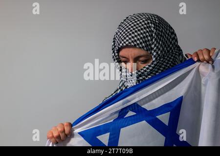 Donna dagli occhi verdi con un velo palestinese che porta una bandiera israeliana. Concetto di conflitto Foto Stock