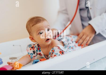 Un bambino carino riceve un'assistenza sanitaria attenta da uno specialista in una clinica calma. Medico controllo bambino utilizzando stetoscopio, fornendo assistenza sanitaria necessaria. Foto Stock