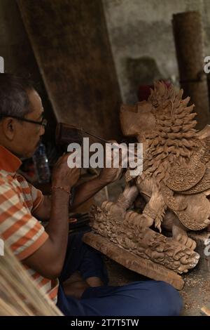 Un uomo scolpisce una statua in legno in officina. Sculture in legno Bali. Foto Stock