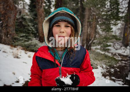 Ragazzo sorridente con cappotto rosso che mangia neve in inverno Foto Stock