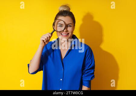 La donna curiosa sta guardando attraverso la lente d'ingrandimento con grande interesse, esaminando qualcosa da vicino Foto Stock