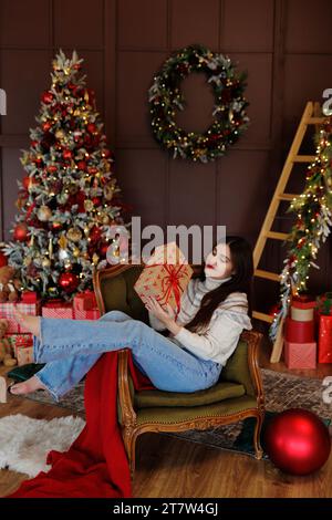 Donna in jeans e maglione che siede su una sedia con regalo rosso Foto Stock