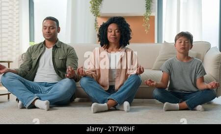 Famiglia calma pacifica multirazziale i genitori afroamericani insegnano meditazione figlio bambino con gli occhi chiusi fanno esercizio yoga mamma papà e bambino piccolo Foto Stock