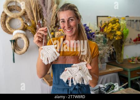 Fiorista che mostra appendiabiti fatti a mano in macrame nel suo negozio Foto Stock