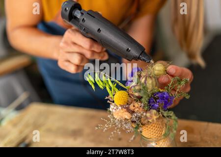 Primo piano delle mani utilizzando una pistola per colla per assemblare una disposizione floreale in un cono Foto Stock