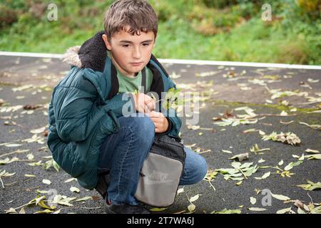 Un giovane ragazzo, all'inizio dell'adolescenza, che affronta le sfide dell'autismo, un momento di angoscia sul marciapiede, che esprime le sue emozioni in un crollo Foto Stock