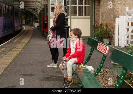 Una scena che riscalda il cuore si svolge nei panni di un bambino di 6 anni e di sua madre single, in attesa pazienza dell'arrivo del treno Foto Stock