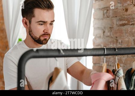 L'uomo sta sfogliando le sue varie camicie appese al portabiti nel guardaroba Foto Stock