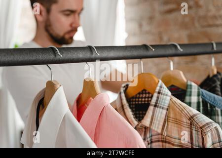 L'uomo sta sfogliando le sue varie camicie appese al portabiti nel guardaroba Foto Stock