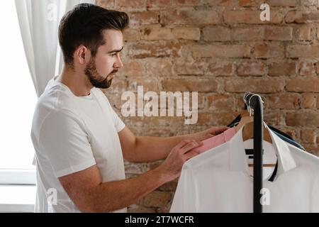 L'uomo sta sfogliando le sue varie camicie appese al portabiti nel guardaroba Foto Stock