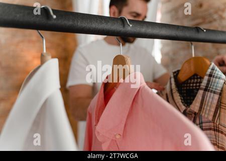 L'uomo sta sfogliando le sue varie camicie appese al portabiti nel guardaroba Foto Stock