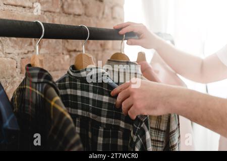 L'uomo sta sfogliando varie camicie appese al portabiti nel guardaroba Foto Stock