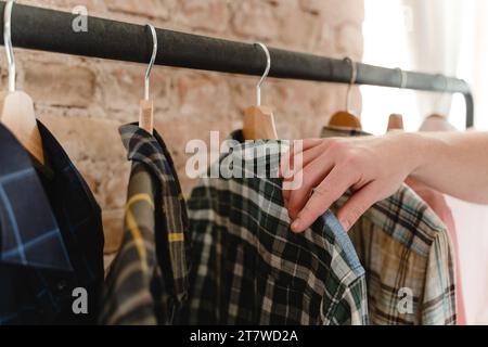 L'uomo sta sfogliando varie camicie appese al portabiti nel guardaroba Foto Stock