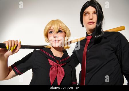 un paio di cosplayer in parrucche e uniformi scolastiche con mazze da baseball che guardano lontano dalla sottocultura grigia Foto Stock