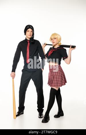 per tutta la lunghezza dei giovani cosplayer in uniforme scura scolastica e parrucche con mazze da baseball bianche Foto Stock