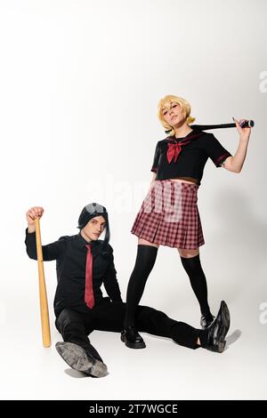 uomo con parrucca nera seduto con mazza da baseball vicino a una donna in uniforme scolastica con tendenza cosplay bianca Foto Stock