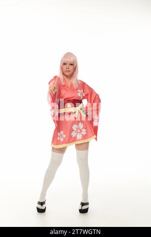 donna intera in parrucca bionda e kimono rosa che punta alla fotocamera sulla cultura cosplay bianca Foto Stock