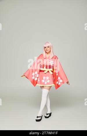 intera lunghezza di giovane donna anime in parrucca bionda e kimono rosa su sottocultura grigia giapponese Foto Stock