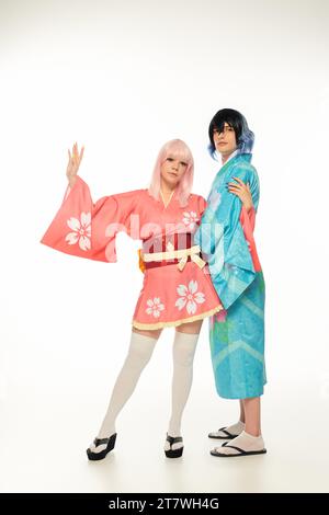 giovane donna in kimono che salta la mano vicino a un uomo in stile anime in parrucca su una moda di sottocultura asiatica bianca Foto Stock