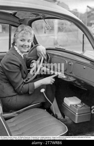 Negli anni '1950 Una giovane donna in un'auto che utilizza alcune delle funzioni extra installate, premendo un pulsante sul cruscotto e attivando un dispositivo sconosciuto. 1957 Foto Stock