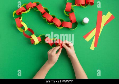 le mani delle ragazze fanno catena di carta per la decorazione di natale di capodanno dyi occupazione facile a casa Foto Stock