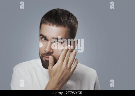Giovane uomo sta applicando crema idratante sul suo viso Foto Stock
