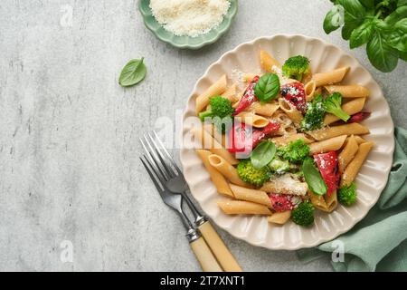 Penne per pasta integrale con broccoli e peperone rosso grigliato e su sfondo grigio chiaro ardesia, pietra o cemento. Pasta vegana. Tradizionale Itali Foto Stock