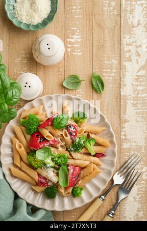 Penne per pasta integrale con broccoli e peperoni rossi grigliati e su un tavolo rustico in legno chiaro. Pasta vegana. Cucina tradizionale italiana Foto Stock