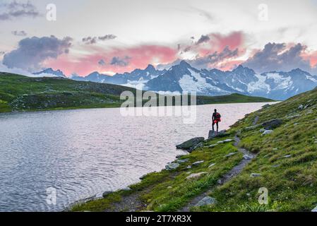 L'escursionista si trova vicino alla riva del lago Fenetre ammirando il tramonto sul massiccio del Monte Blanc, valle del Ferret Foto Stock