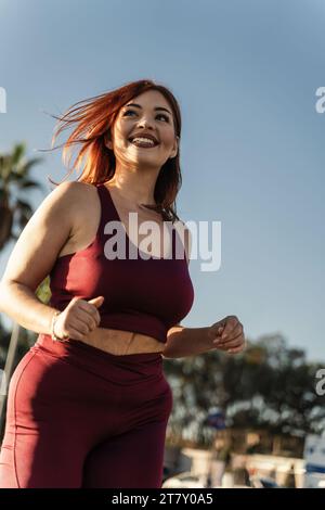 Una donna vivace si diverte a correre in un parco cittadino, mostrando la sua routine di fitness e l'energia di uno stile di vita attivo Foto Stock