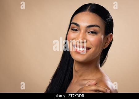 Ritratto di donna birazziale con capelli scuri, sorridente e trucco naturale su sfondo marrone Foto Stock