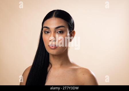 Ritratto di donna birazziale con capelli scuri e trucco naturale su sfondo marrone Foto Stock