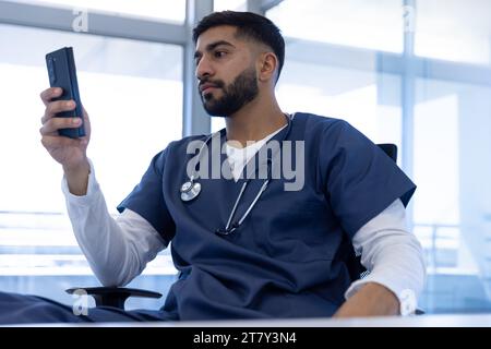 Medico maschio birazziale che utilizza lo smartphone in ufficio ospedaliero Foto Stock