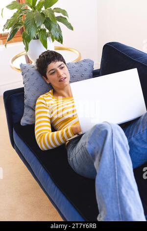 Felice donna birazziale sdraiata sul divano che usa un computer portatile a casa Foto Stock