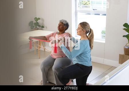 Fisioterapista femminile caucasica e paziente afrcia americana anziana con banda, spazio copia Foto Stock